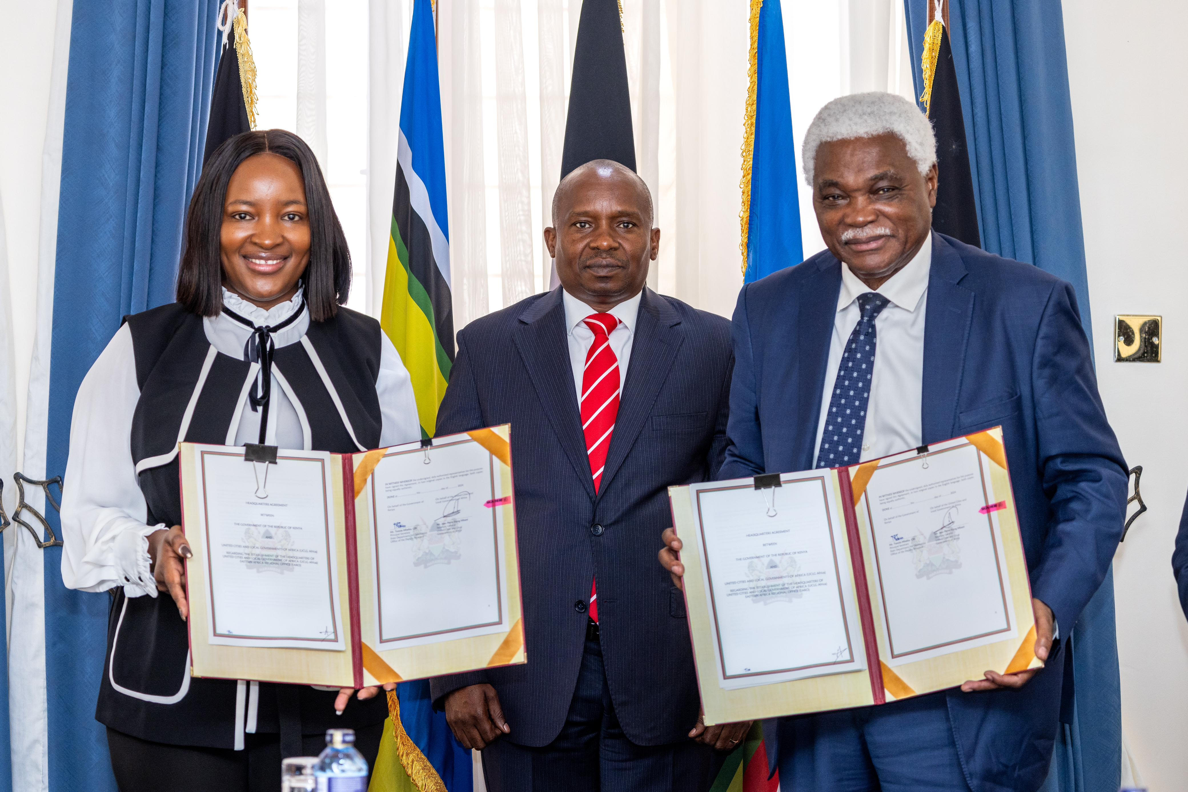 Deputy President Prof. Kithure Kindiki (center) poses with Principal Secretary for Devolution Teresia Mbaika and the UCLG Africa Secretary General, Jean-Pierre Elong Mbassi during the signing of the Hosting Agreement for the East Africa Regional Office.
