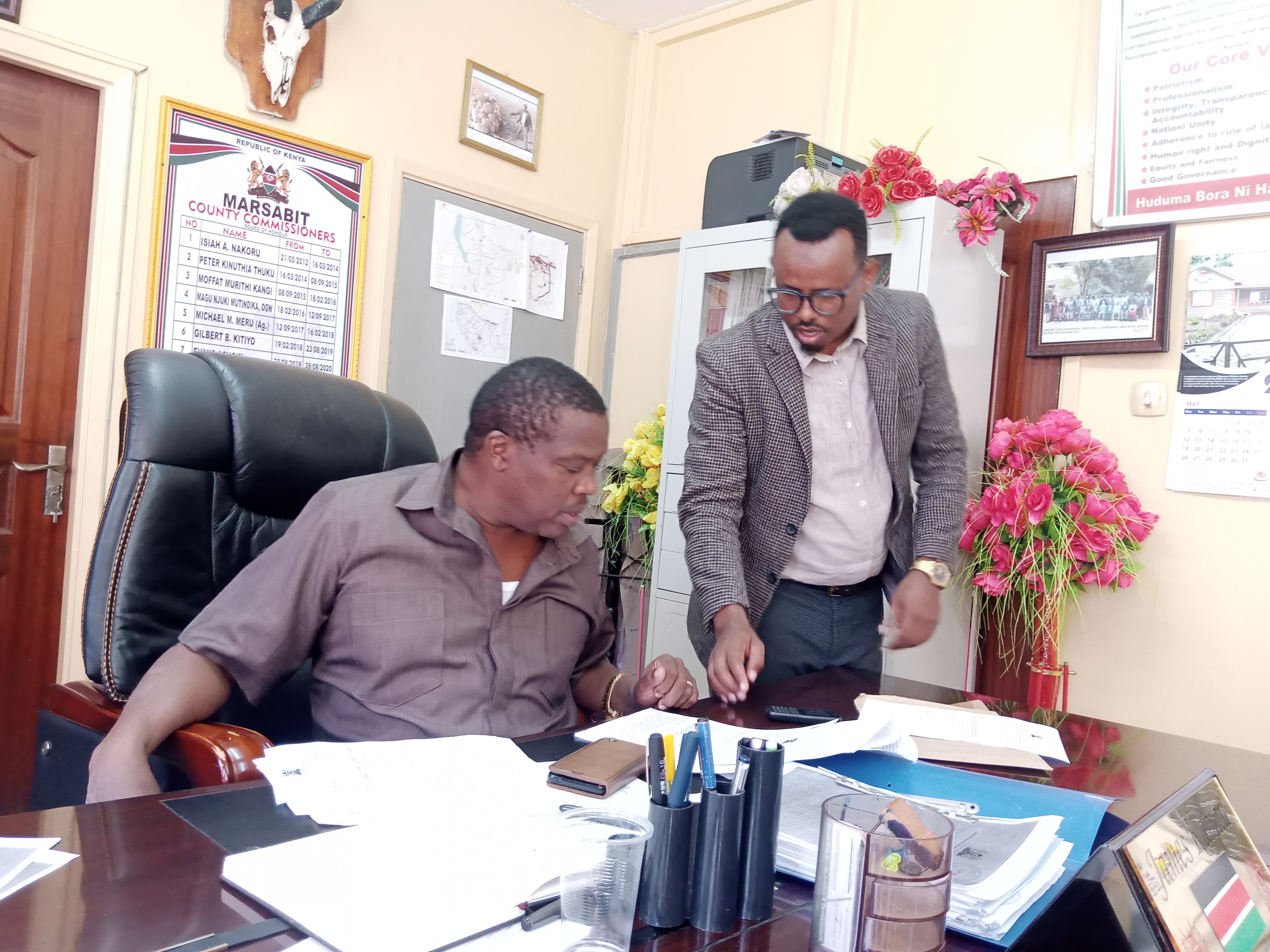Marsabit County Commissioner James Kamau  compares notes with  the county coordinator for NACADA in his office over the status of the  fight against the smuggling of contrabands that include drugs and   counterfeit alcoholic drinks from a neighbouring country. 