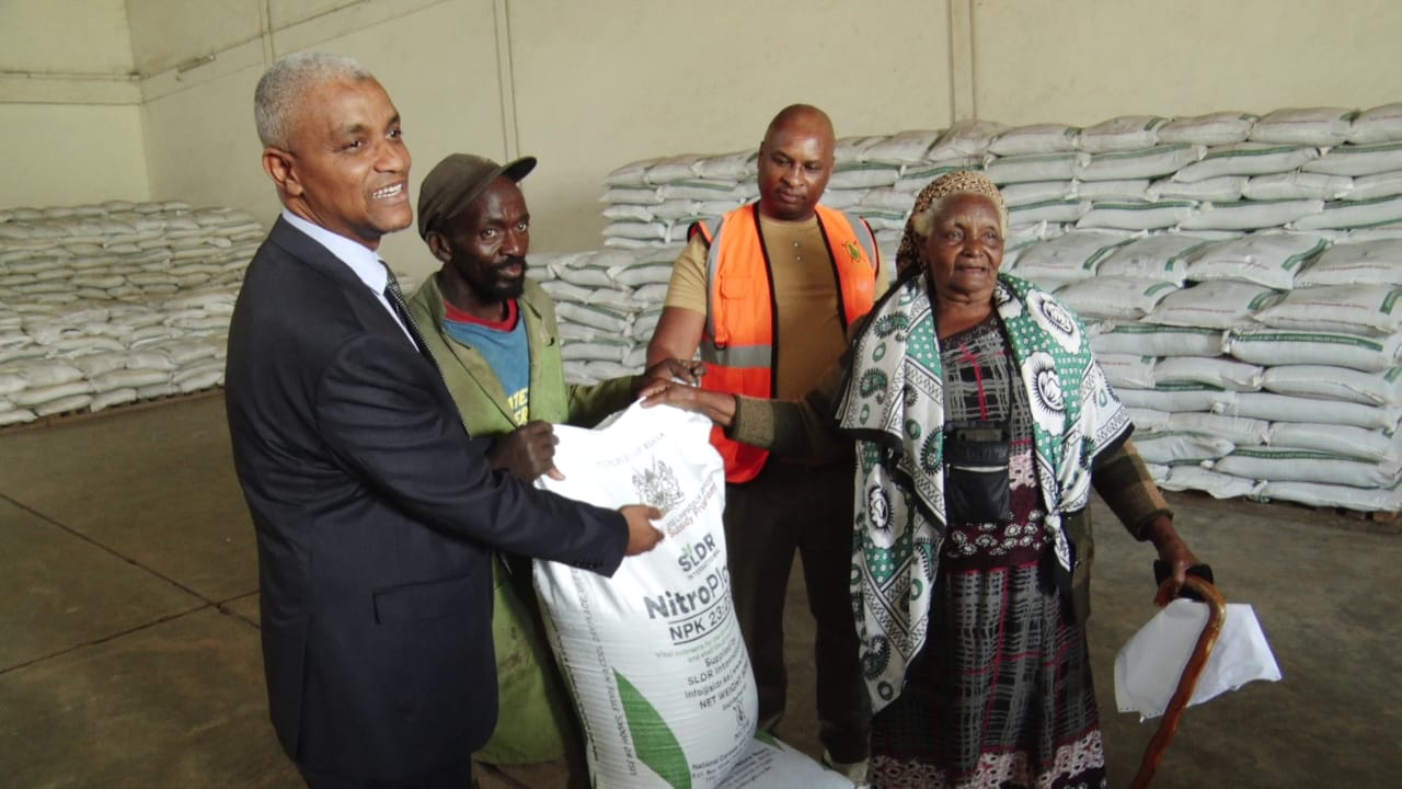 The National Fertilizer Technical Committee Chairman Haron Khator (left) presents a Thika farmer with subsidized fertilizer she had purchased at the National Cereals and Produce Board in Thika town .