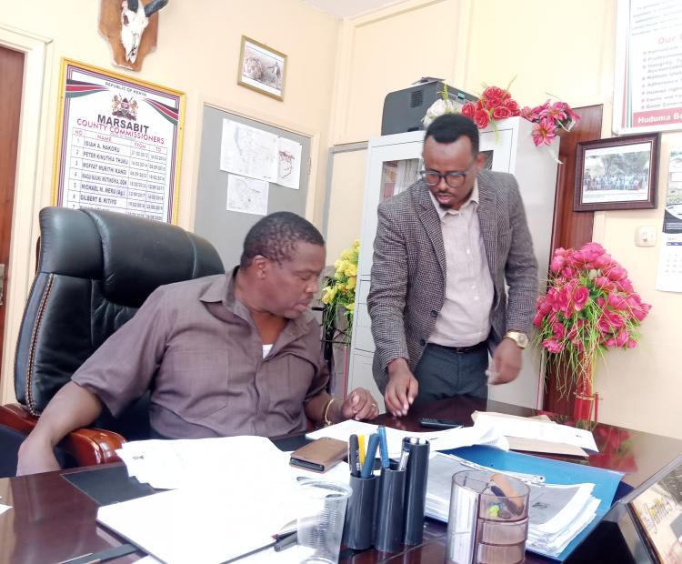 Marsabit County Commissioner James Kamau  compares notes with  the county coordinator for NACADA in his office over the status of the  fight against the smuggling of contrabands that include drugs and   counterfeit alcoholic drinks from a neighbouring country. 